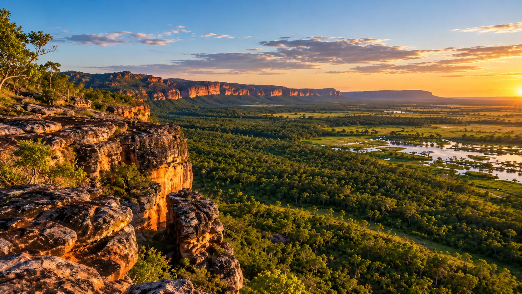 AI-generated panoramic landscape inspired by Kakadu National Park, showing golden sandstone cliffs, dense green woodland and reflective wetlands beneath a warm sunset sky in Australia's Northern Territory.
