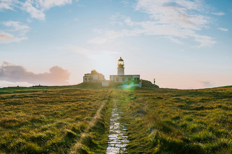 Neist Point Lighthouse at sunset on the Isle of Skye, with warm light over cliffs and open Atlantic water.
