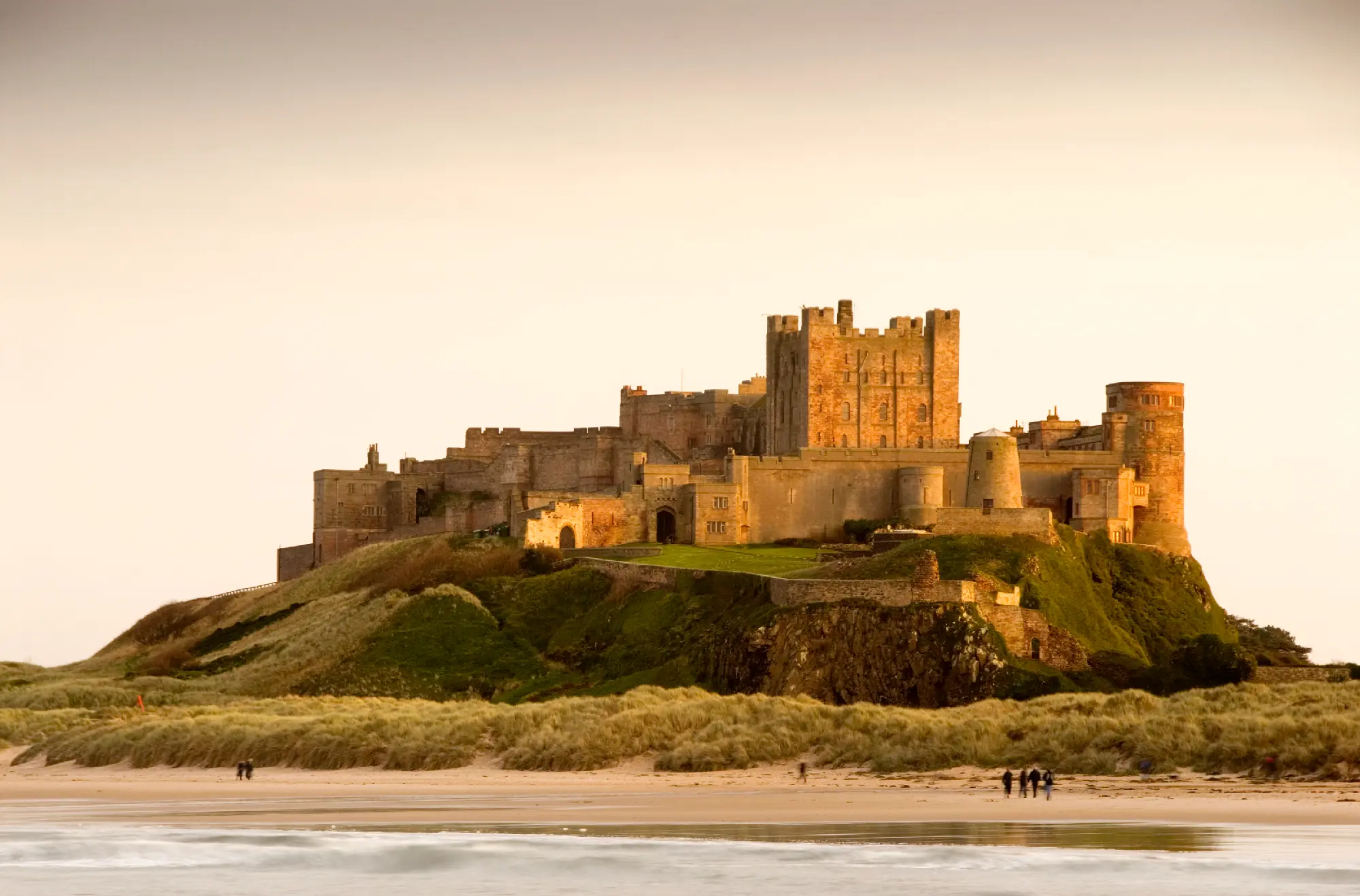 Bamburgh Castle overlooking the beach and sand dunes on the Northumberland coast of England at dusk.