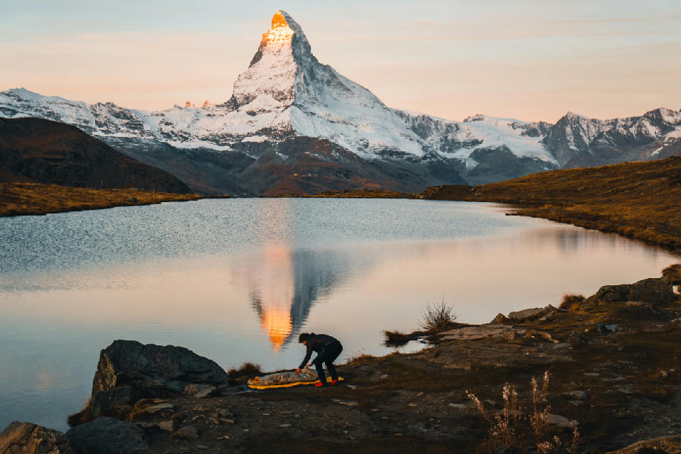 Matterhorn reflected in Stellisee at sunrise with person on the lakeshore, Zermatt, Switzerland.