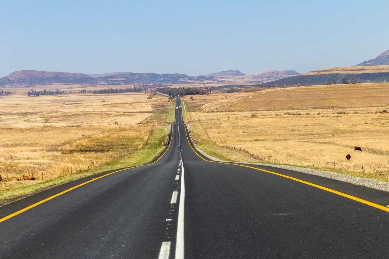 Long straight road crossing the semi-arid Klein Karoo landscape with distant mountains and open desert plains near Route 62 in South Africa.