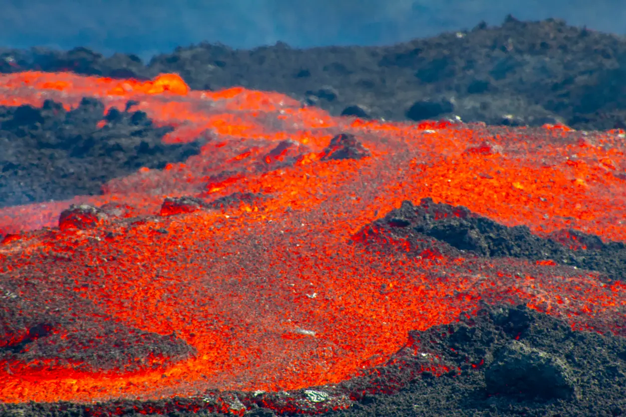 Bright orange lava flowing across black volcanic rock at Fagradalsfjall eruption site on the Reykjanes Peninsula, Iceland.