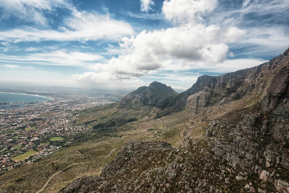 Rocky cliffs of Table Mountain in the foreground looking toward Devil’s Peak and Cape Town suburbs and coastline below.