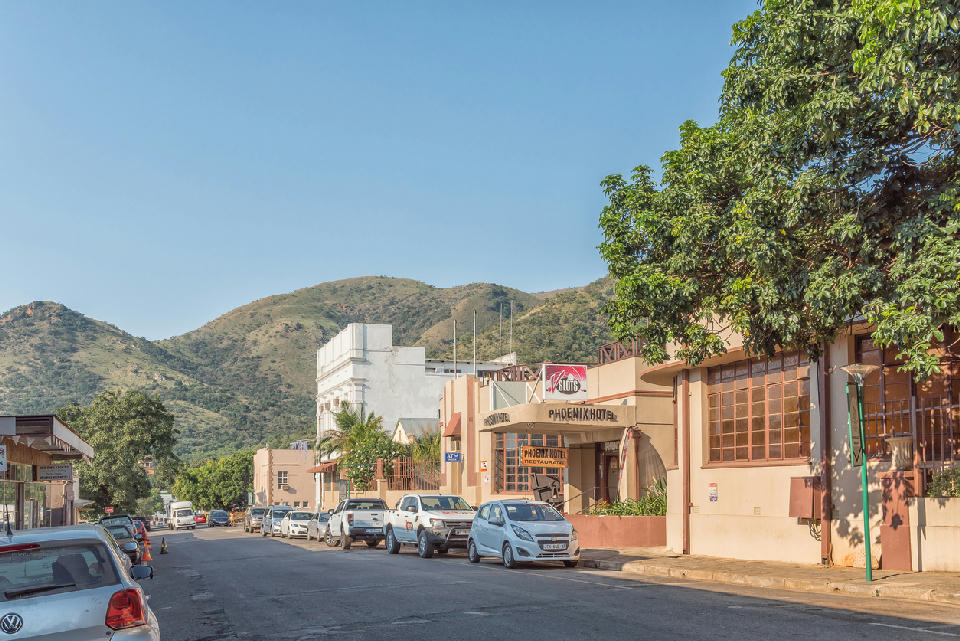 Street scene in Barberton with historic buildings, parked vehicles and the Makhonjwa Mountains rising behind the town.
