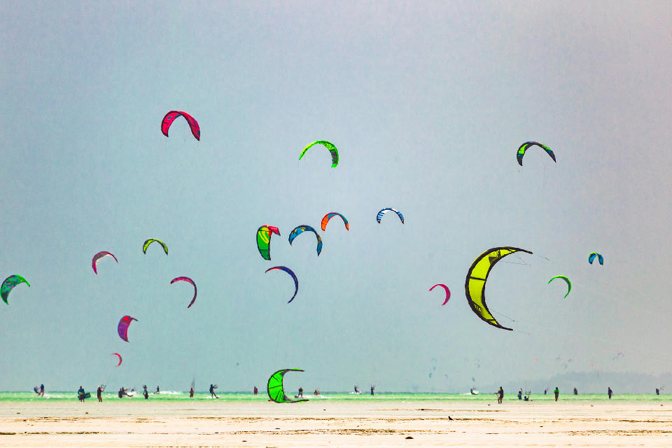 Colourful kites flying above kitesurfers on the shallow lagoon at Paje Beach, Zanzibar, Tanzania.