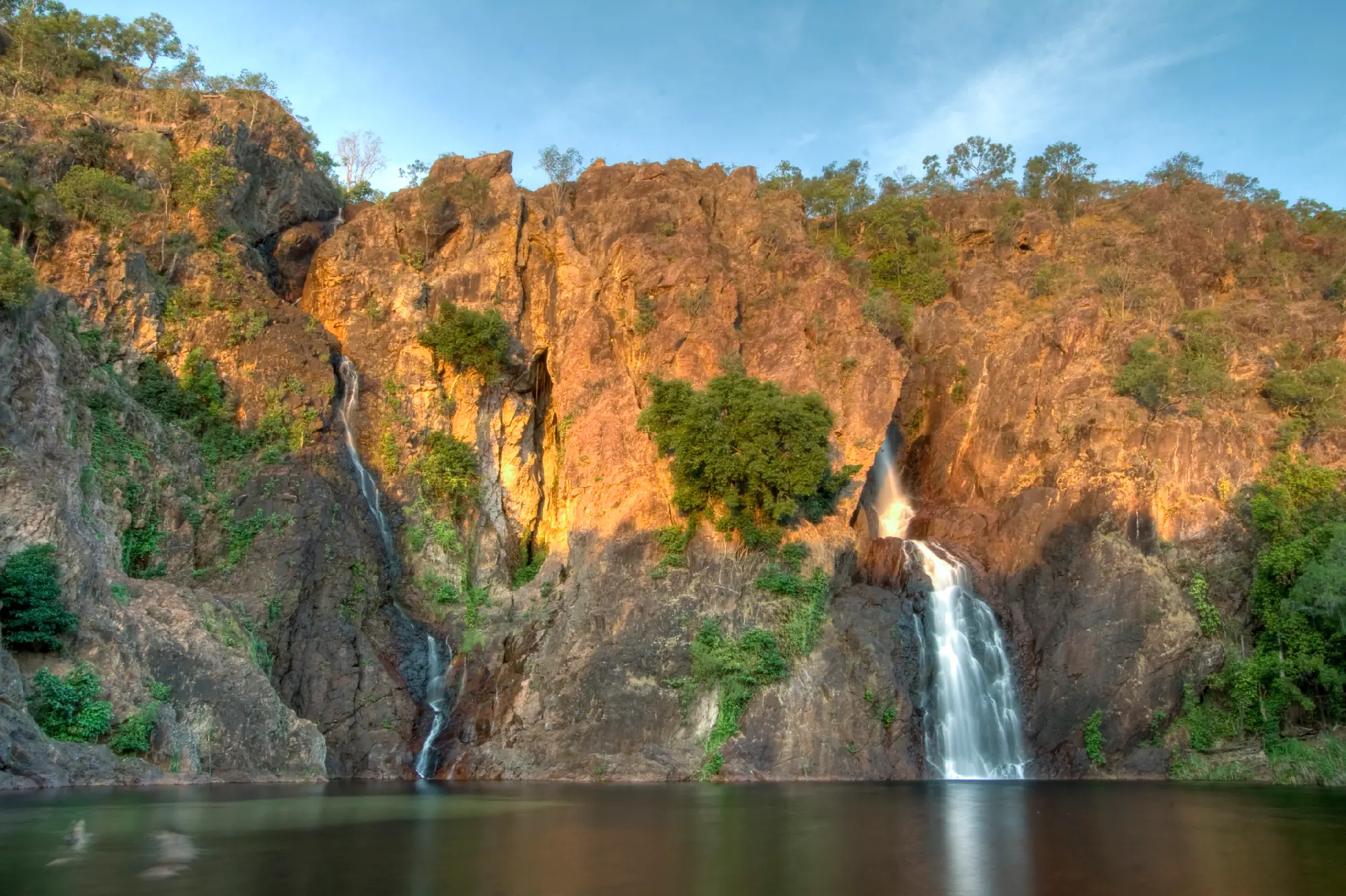Twin waterfalls descending sunlit rocky cliffs into a calm plunge pool at Wangi Falls in Litchfield National Park, Northern Territory, Australia.