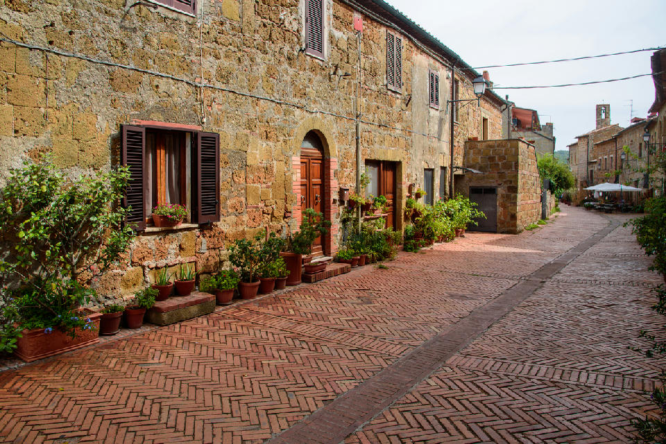 Stone houses and brick-paved street with potted plants in the historic village of Sovana, Tuscany, Italy.