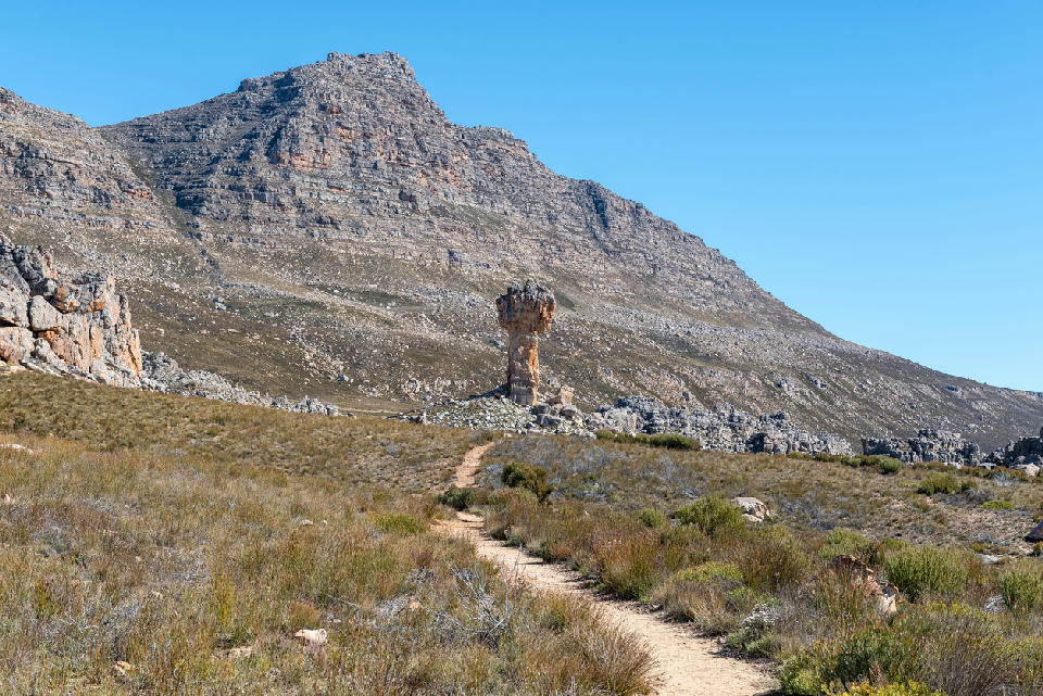 Hiking trail leading towards the Maltese Cross rock formation in the Cederberg Mountains, surrounded by rugged sandstone slopes and mountain scenery beneath a clear blue sky.