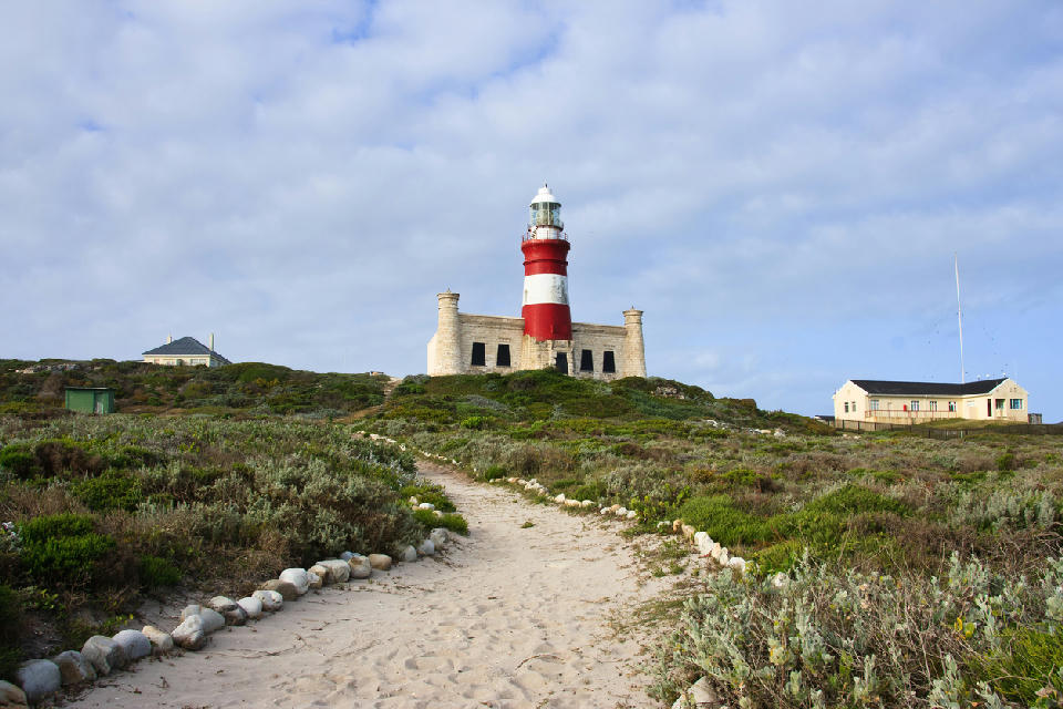 Cape Agulhas Lighthouse above coastal fynbos and sandy pathway at the southernmost point of Africa, South Africa.