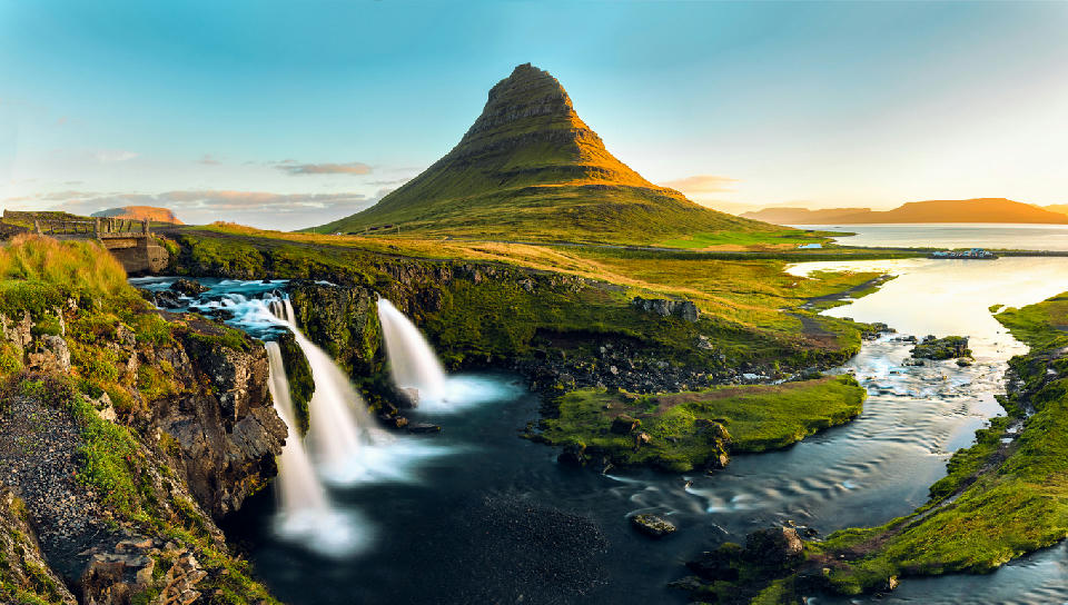 Kirkjufell mountain on the Snæfellsnes Peninsula in Iceland, with Kirkjufellsfoss waterfall flowing into a river under clear evening light.