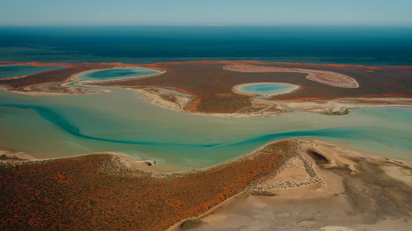 Aerial view of turquoise lagoons, tidal channels and red arid coastline at Shark Bay, Western Australia.