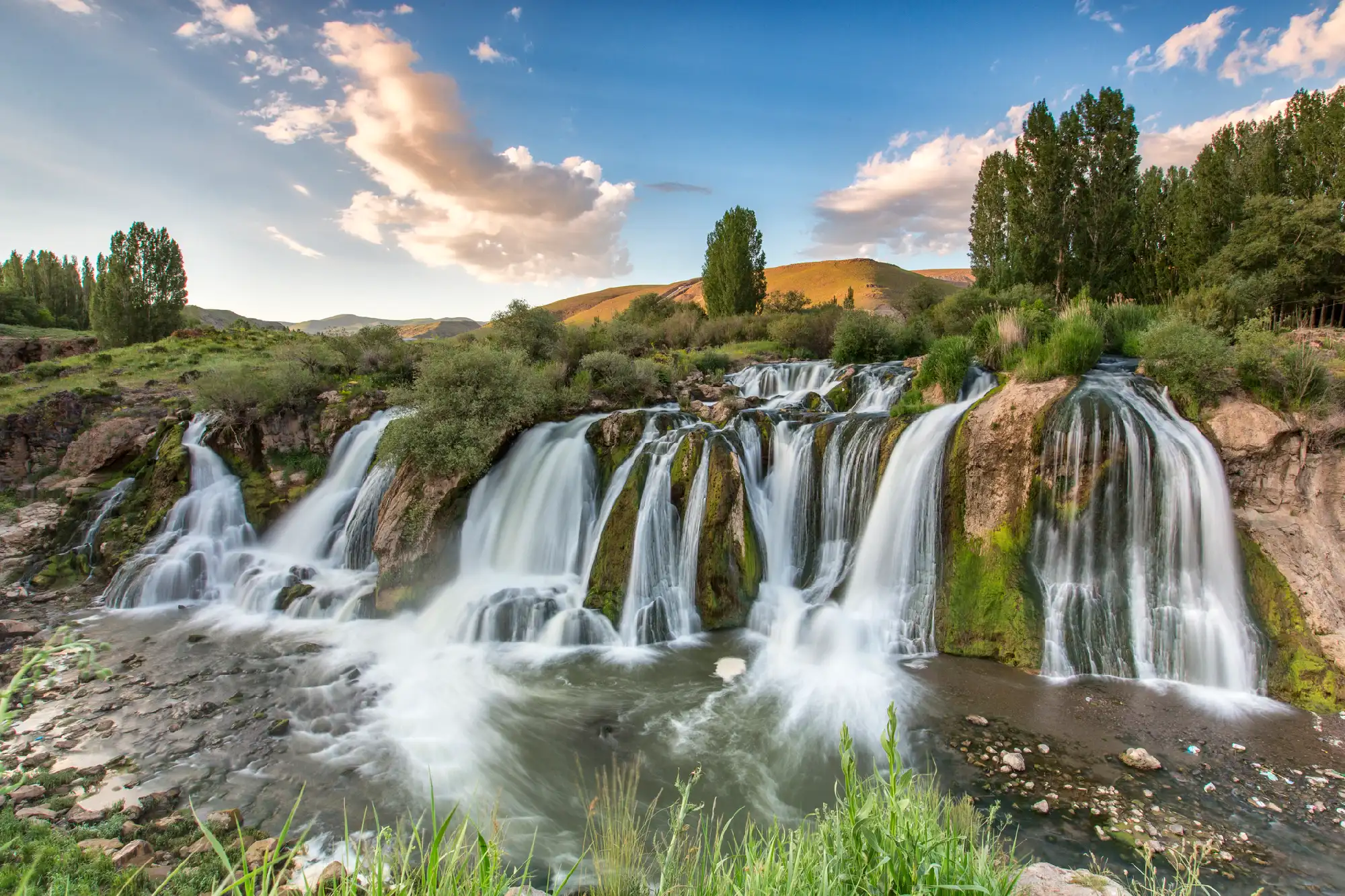 Wide view of Muradiye Waterfall flowing over multiple rocky cascades surrounded by green vegetation in Van Province, Turkey.