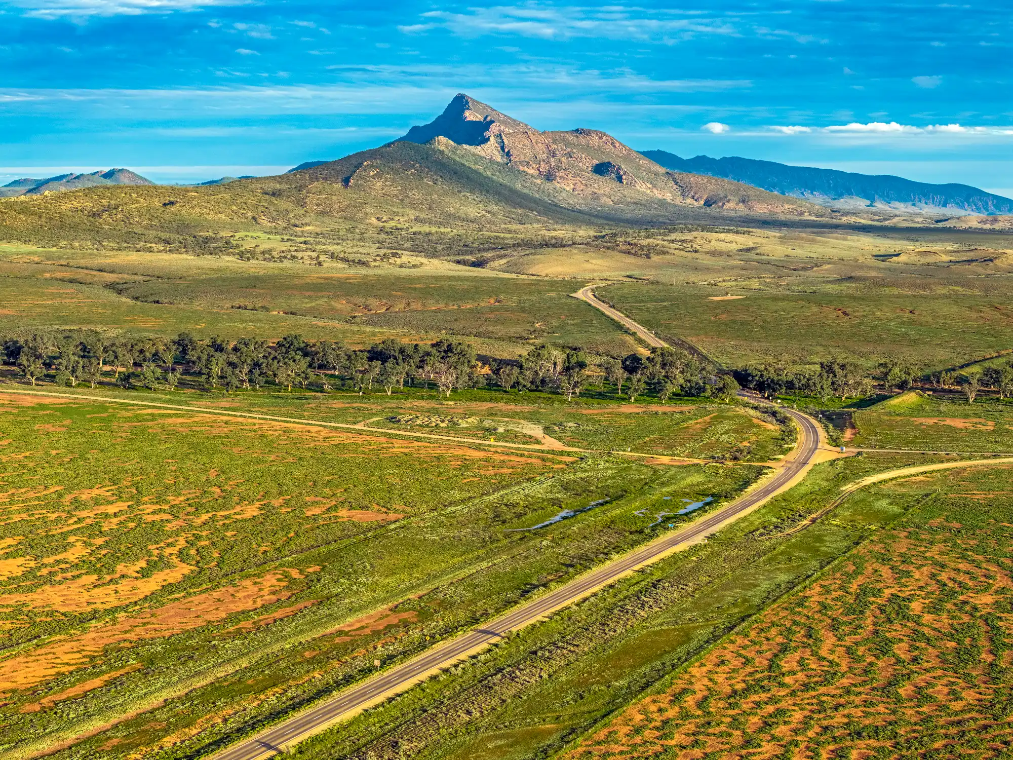 Aerial landscape of Mount Aleck and the green Flinders Ranges plains, with winding roads and tree-lined Moralana Creek near Moralana Scenic Drive, South Australia.