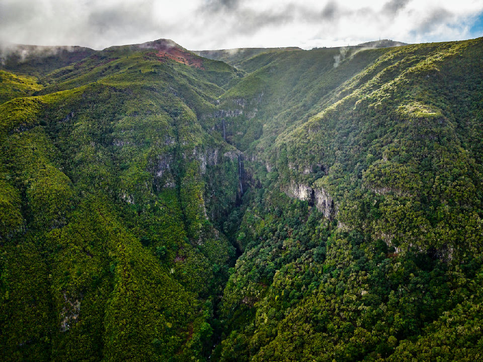 Aerial view of Risco Waterfall cascading into a deep, forested ravine in the Rabaçal valley, Madeira.