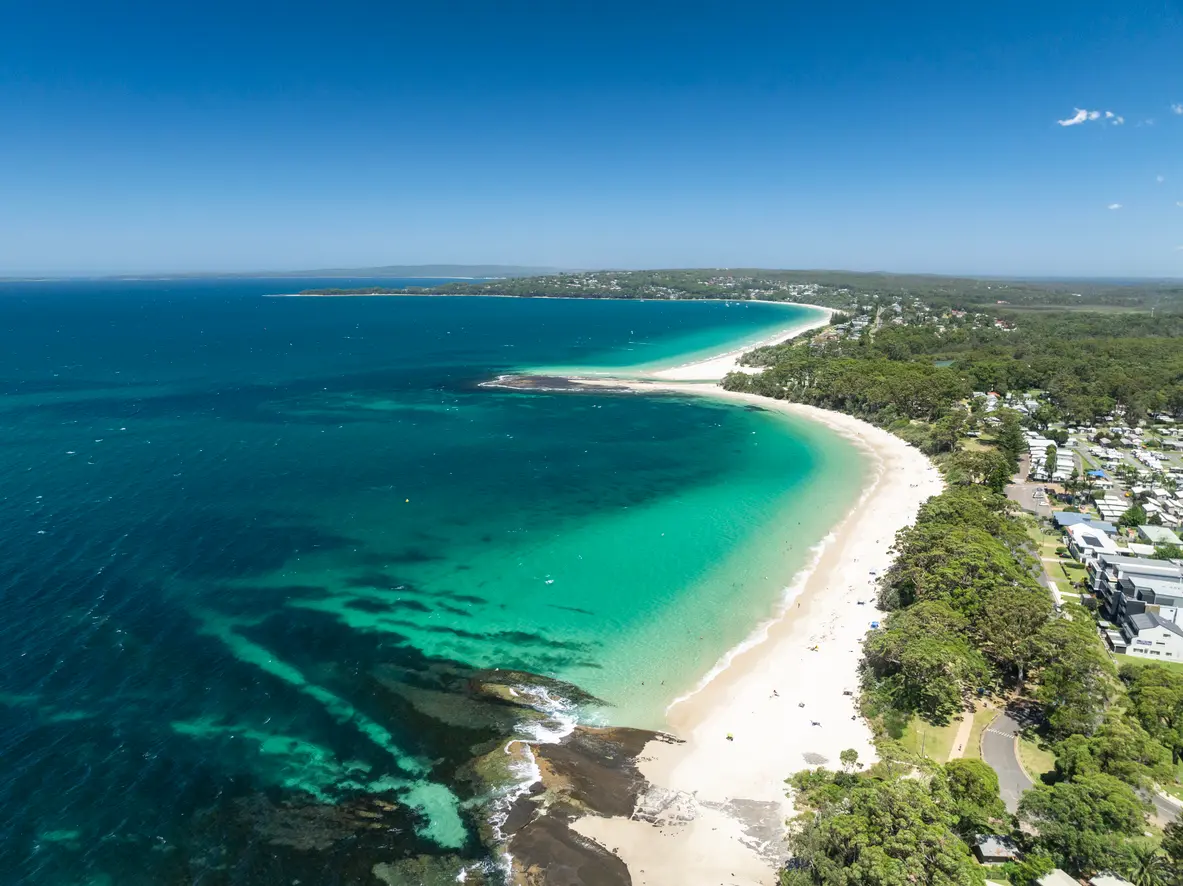 Sweeping aerial view across Jervis Bay with turquoise water, white-sand beaches and the coastal communities of Huskisson and Vincentia.