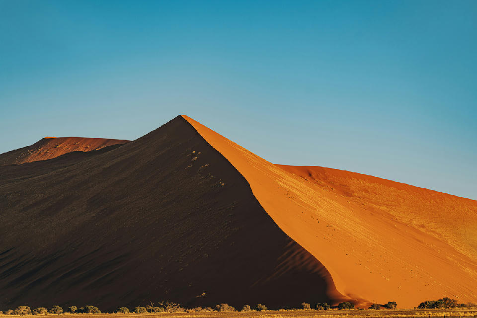 Sunlit crest and deep shadow on Dune 45 in the Sossusvlei desert of Namibia beneath a clear blue sky.