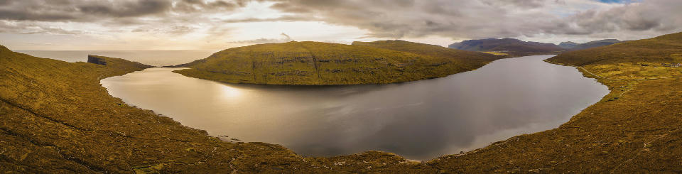 Panoramic view of Sørvágsvatn lake on Vágar Island, Faroe Islands, with the Atlantic Ocean visible beyond the coastal plateau.