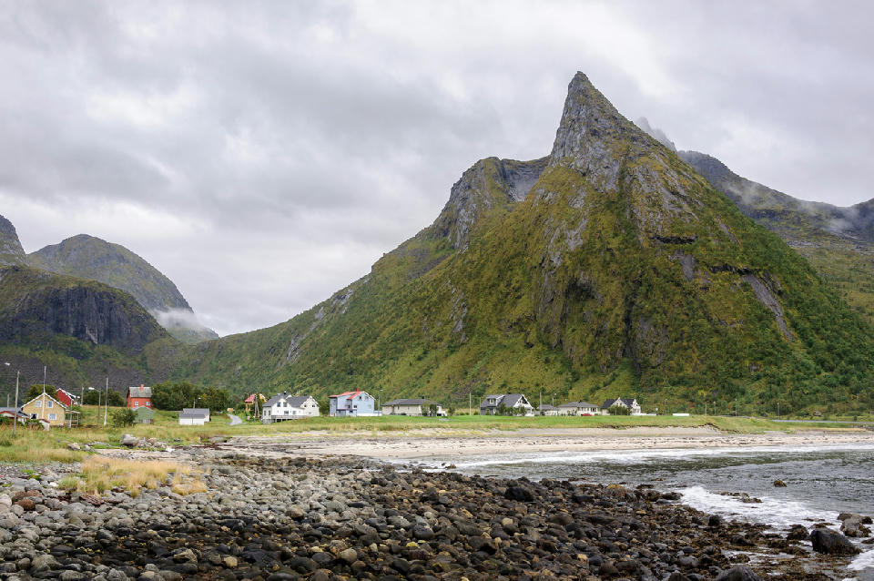 Rocky and sandy shoreline at Ersfjord with village houses at the base of a sharply rising green mountain ridge