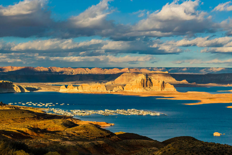 Wahweap Overlook view of Wahweap Marina at Lake Powell in Page, Arizona, showing houseboats on blue water surrounded by layered sandstone cliffs and desert landscape.