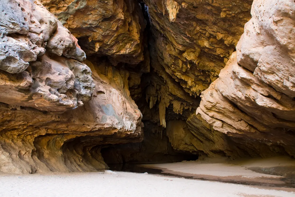 Limestone formations frame the entrance to Tunnel Creek, with a shallow creek disappearing into the dark cave interior.