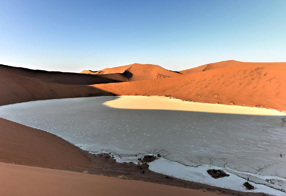 Curved white clay pan enclosed by red sand dunes in Hiddenvlei, Namibia’s Namib Desert.