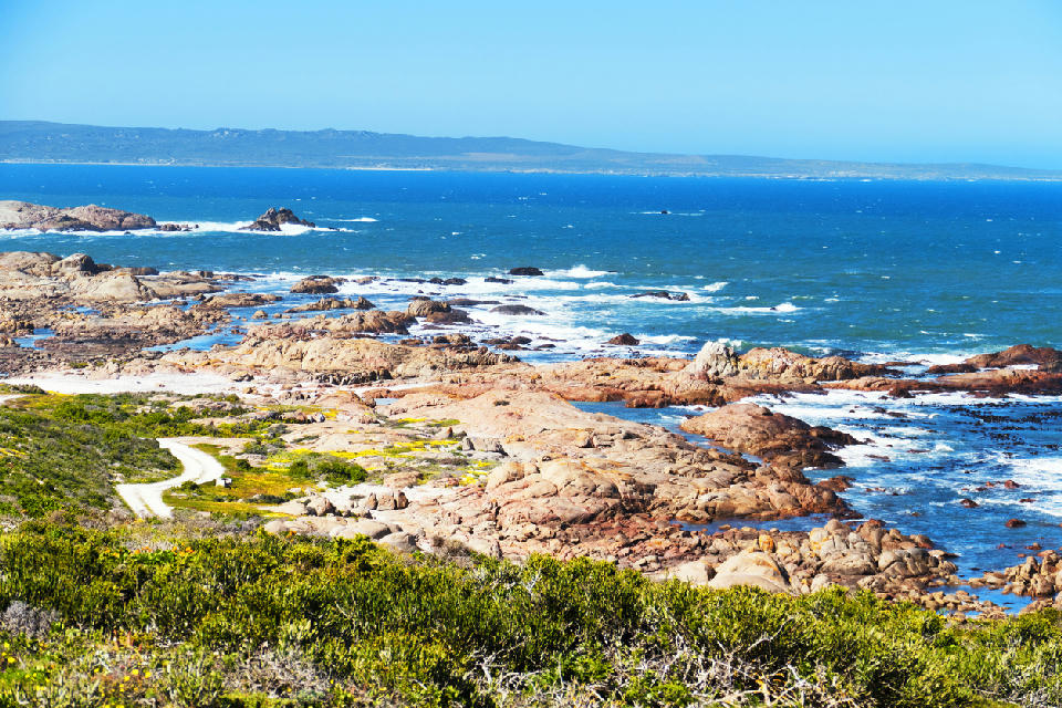 Rocky coastline and granite outcrops at Tietiesbaai in Cape Columbine Nature Reserve near Paternoster, with waves breaking along the Atlantic shoreline and fynbos vegetation in the foreground.