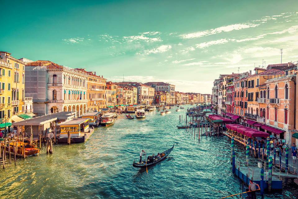 A gondolier paddling toward sunset on the Grand Canal, viewed from the Rialto Bridge in Venice.