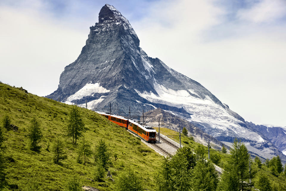 Gornergrat railway train ascending alpine slopes with the Matterhorn rising in the background near Zermatt, Switzerland.