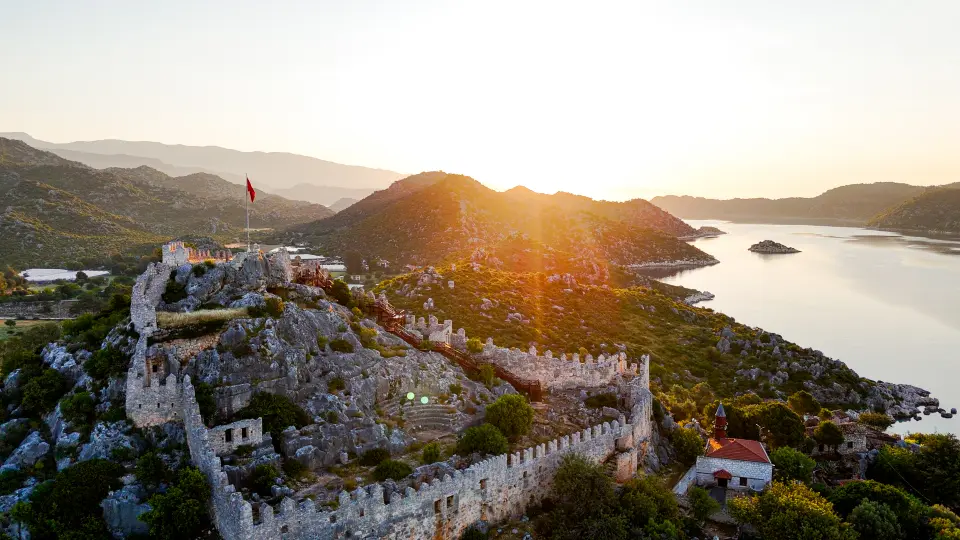 Aerial sunset view of Simena Castle and Kaleköy overlooking the islands and Mediterranean waters of Kekova, Türkiye.