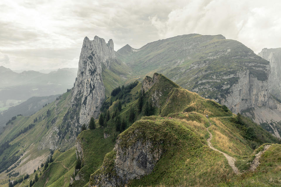 Narrow hiking path along a grassy ridge leading toward the jagged rock formations of Saxer Lücke in the Alpstein mountains, Switzerland.