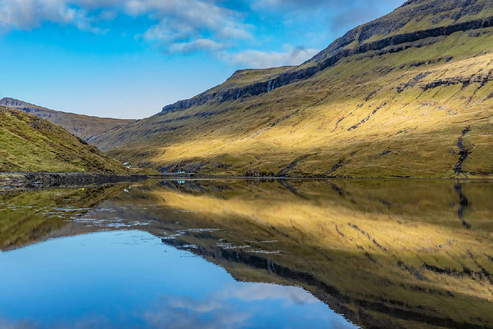 Still water reflections on Leynavatn lake surrounded by terraced hills on Streymoy, Faroe Islands.