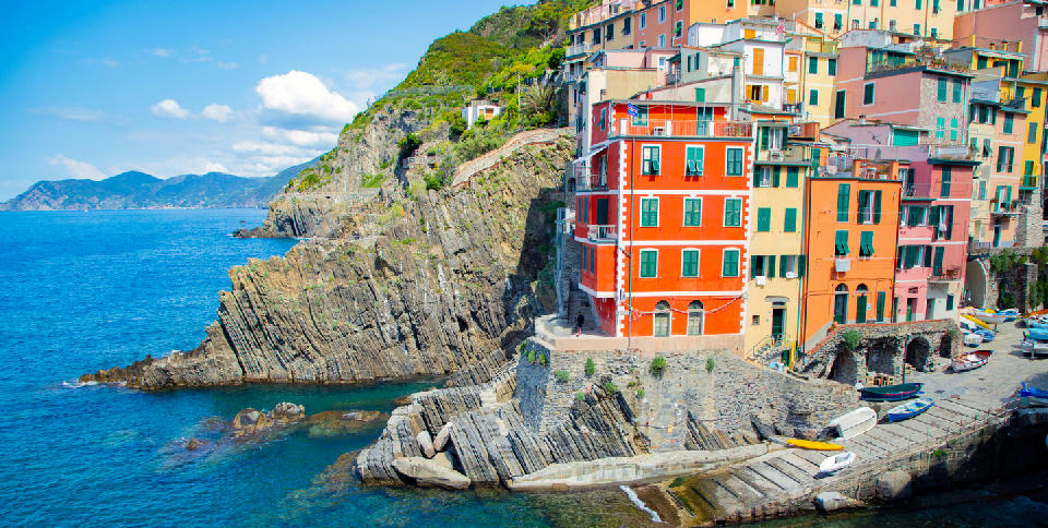 Brightly coloured houses and boats in the harbour of Riomaggiore, along the rugged coastline of Cinque Terre, Italy.
