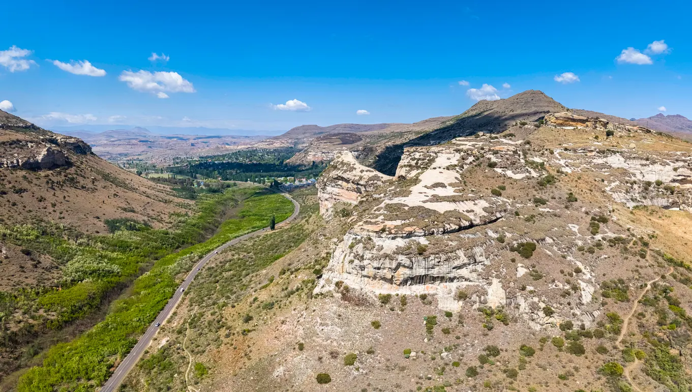Aerial view of sandstone cliffs and a winding valley road leading towards Clarens in South Africa's Eastern Highlands.