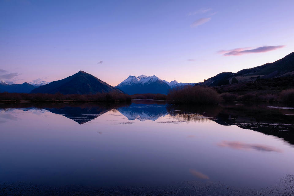Snow-capped mountains reflected in the calm waters of Glenorchy Lagoon at dawn near Glenorchy, South Island, New Zealand.