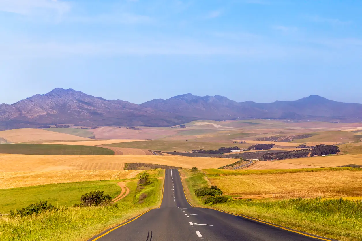 Long road through rolling farmland and mountain landscapes near Stanford in the Overberg region of the Western Cape, South Africa.