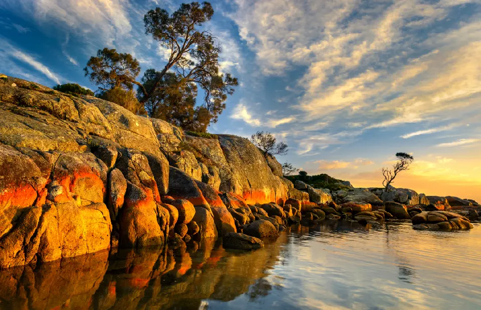 Orange lichen-covered granite rocks and calm coastal water at The Gardens, Bay of Fires, Tasmania.