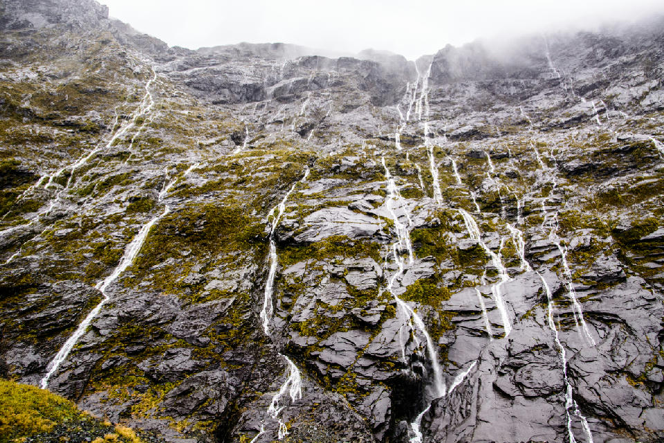 Dozens of temporary waterfalls cascading down steep cliffs in Cleddau Valley near the Homer Tunnel on the Milford Road in Fiordland National Park, New Zealand.