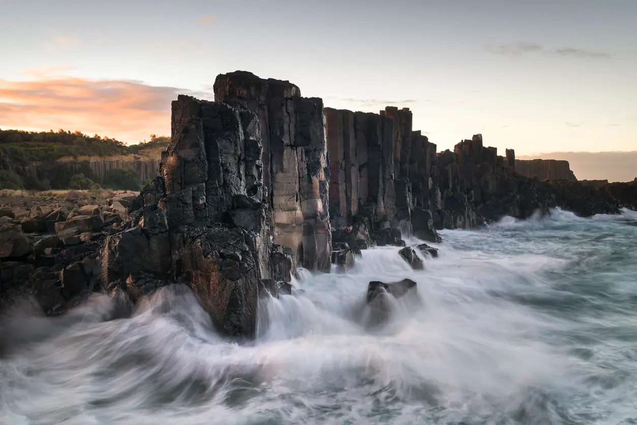 Ocean waves surge around the dark basalt columns of Bombo Headland Quarry at dusk near Kiama, New South Wales.