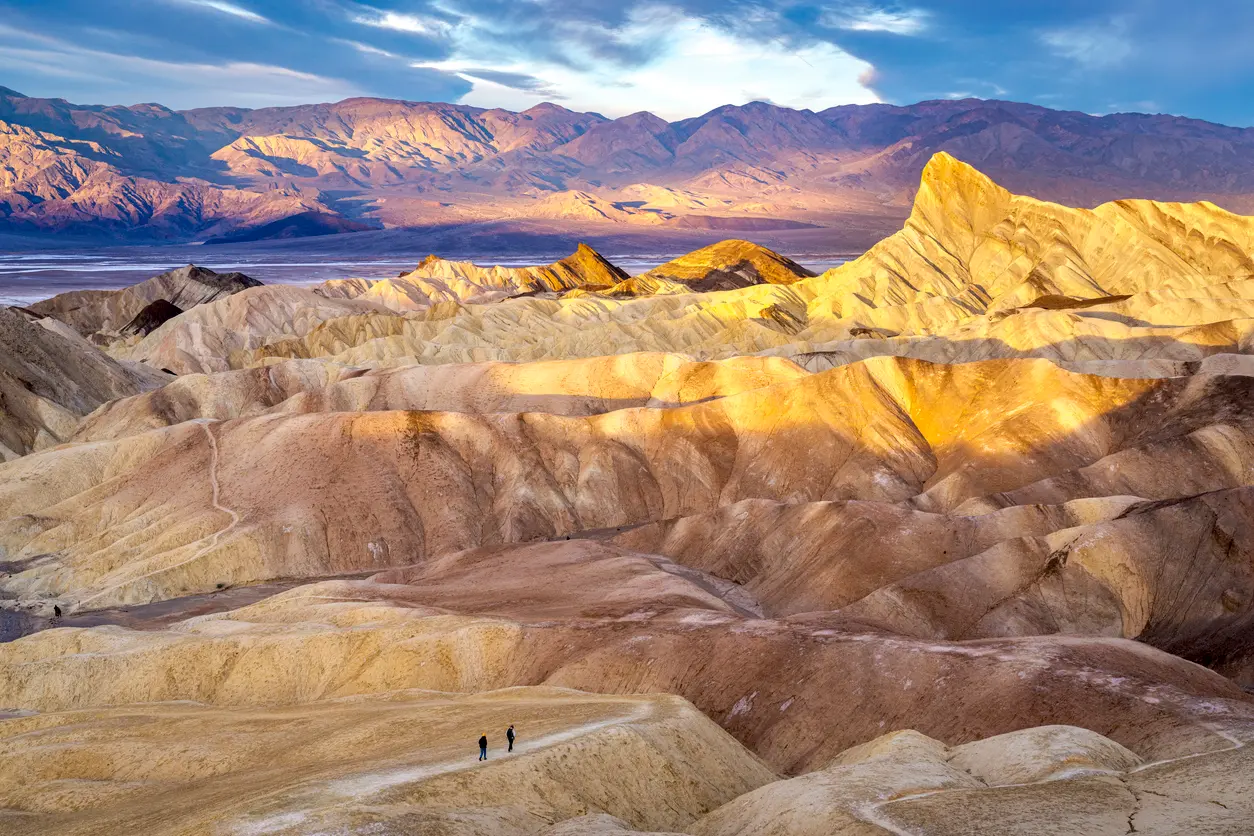 Hikers walking along Zabriskie Point ridges at sunrise in Death Valley National Park California with golden badlands landscape