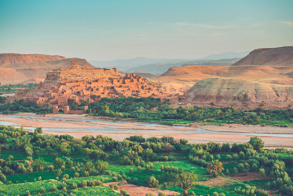 Fortified desert settlement near Ouarzazate, Morocco with the Ounila River, oasis vegetation, and arid canyon landscapes at golden hour