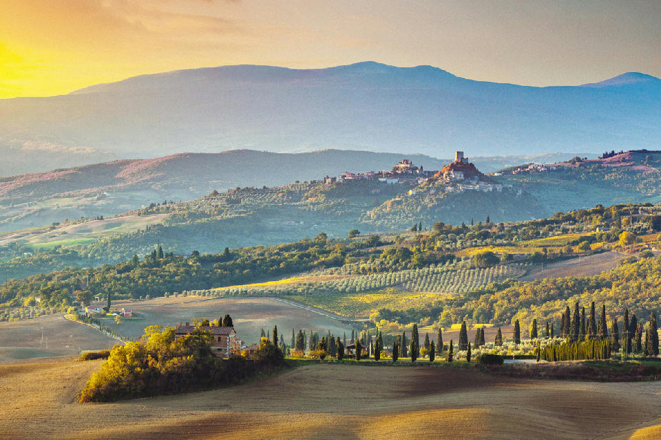 Panoramic view of the rolling hills of Val d’Orcia, with Rocca di Tentennano and the hill town of Castiglione d’Orcia under soft sunrise or sunset light in Tuscany, Italy.