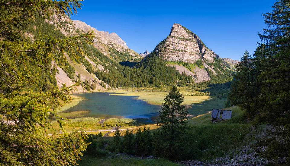 Alpine lake and forested valley with pyramid-shaped mountain in Mercantour National Park, France