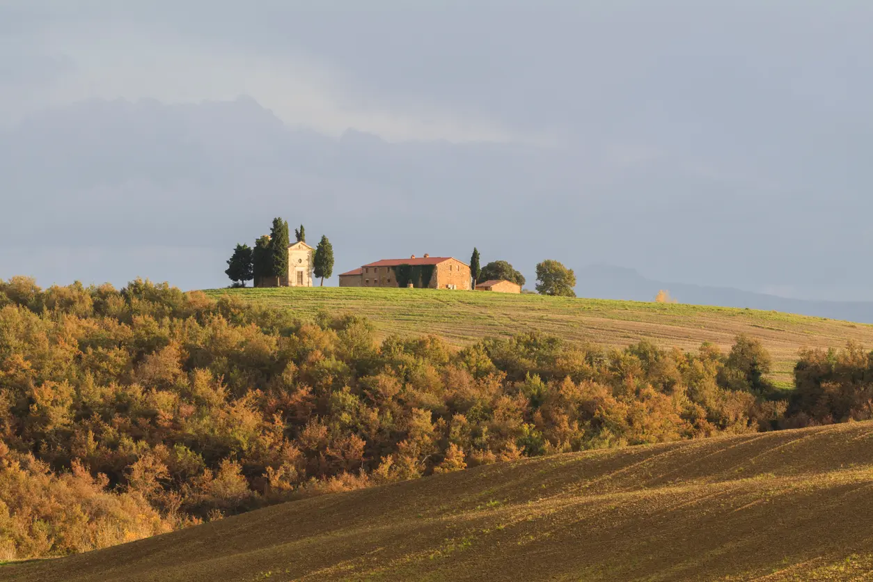 Cappella della Madonna di Vitaleta chapel on a hilltop surrounded by rolling fields and cypress trees in Val d’Orcia, Tuscany, Italy.