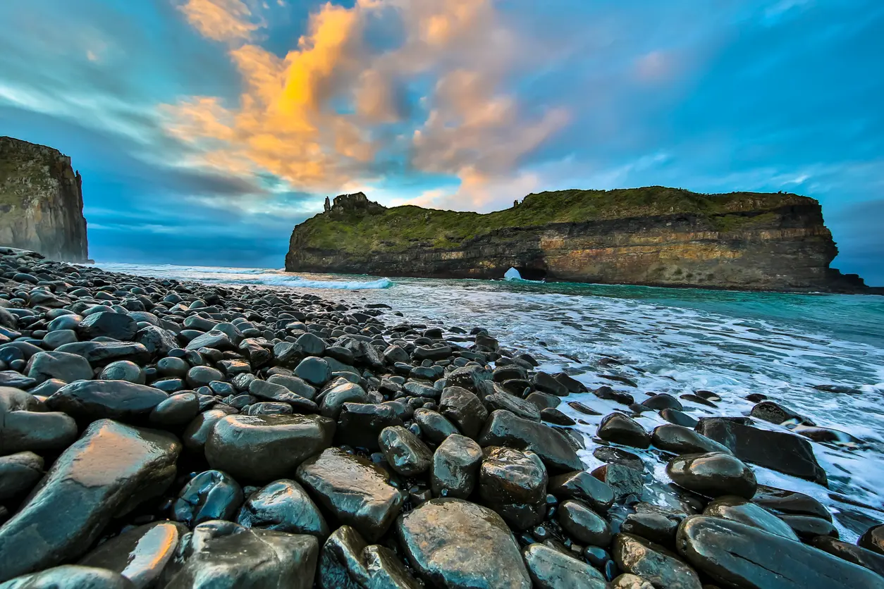 Hole in the Wall sea arch on the Wild Coast of the Eastern Cape, South Africa, viewed from a rocky shoreline beneath colourful clouds and evening light.
