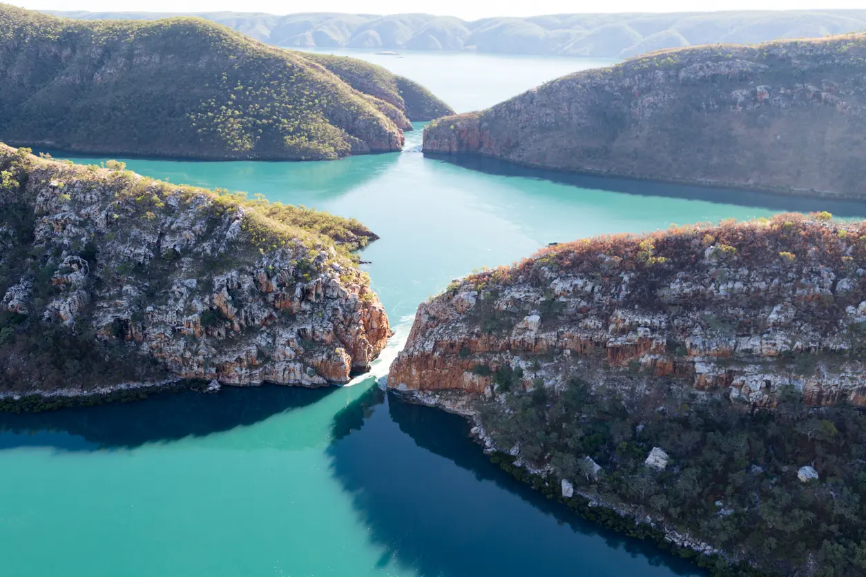 Aerial view of turquoise tidal waters flowing through two narrow gaps in the rugged McLarty Range at Horizontal Falls.