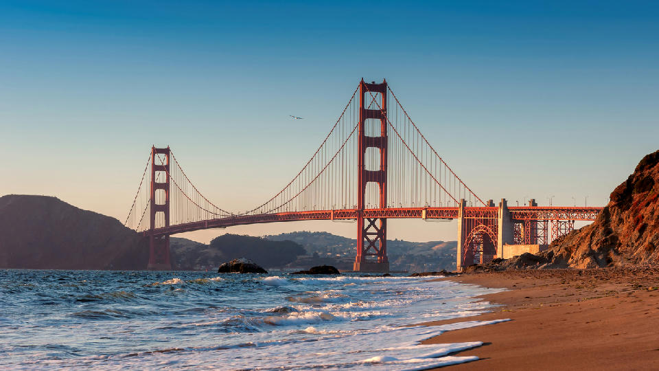 Golden Gate Bridge at sunset viewed from Baker Beach with waves rolling onto the sandy shoreline