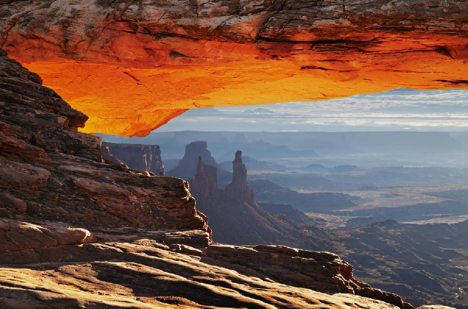 View through Mesa Arch with glowing underside framing distant canyon spires and layered desert terrain in Canyonlands National Park Utah