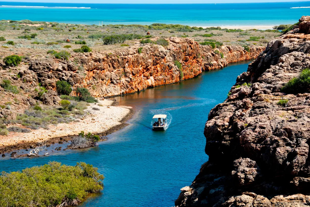 Tour boat travels through Yardie Creek Gorge between rugged red cliffs, with the Ningaloo coast beyond.