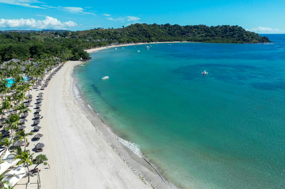 Drone view of Andilana Beach on Nosy Be in Madagascar showing curved white sand beach and turquoise tropical ocean water.