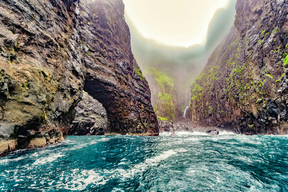 Boat-level view beneath a basalt sea arch inside the Vestmanna bird cliffs with steep canyon walls and turquoise water, Streymoy, Faroe Islands.